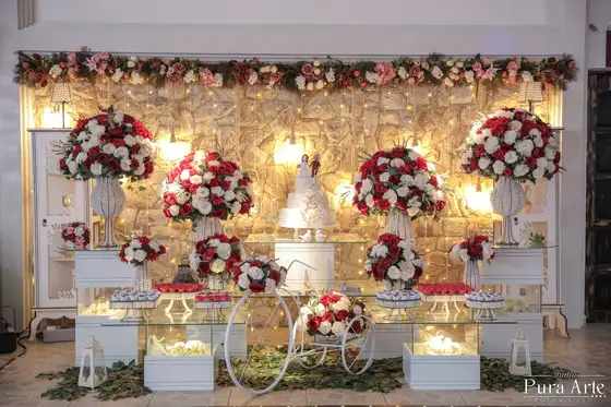 Mesa do bolo com arranjos de rosas vermelhas e brancas